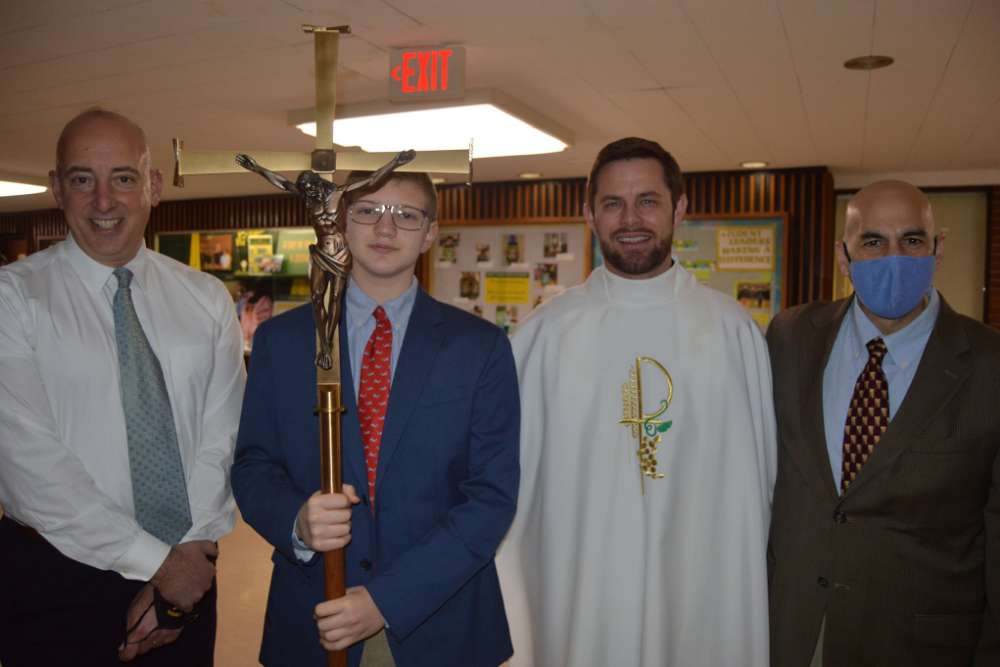 student holding a cross, standing with pastor and teachers